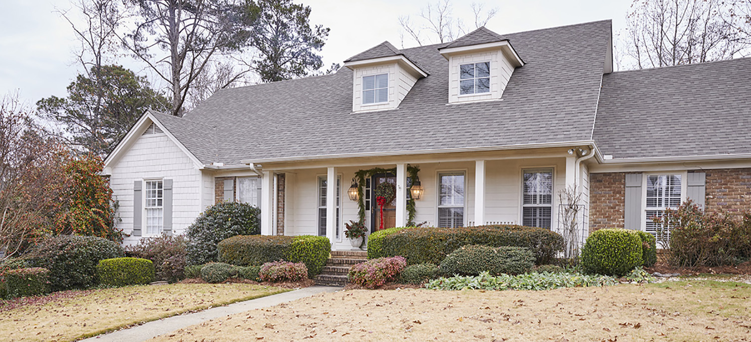 Front elevation photo of home with garland around the front door and a large wreath with a red bow.
